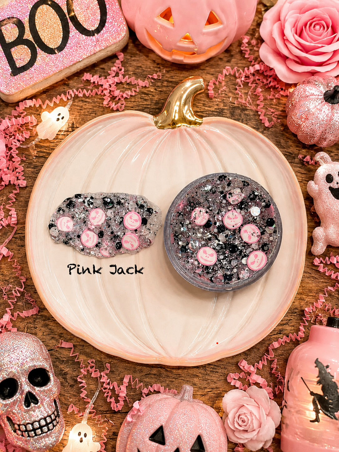 Pink and black Halloween-themed hair glitter with ghost charms in a jar on a pink pumpkin dish
